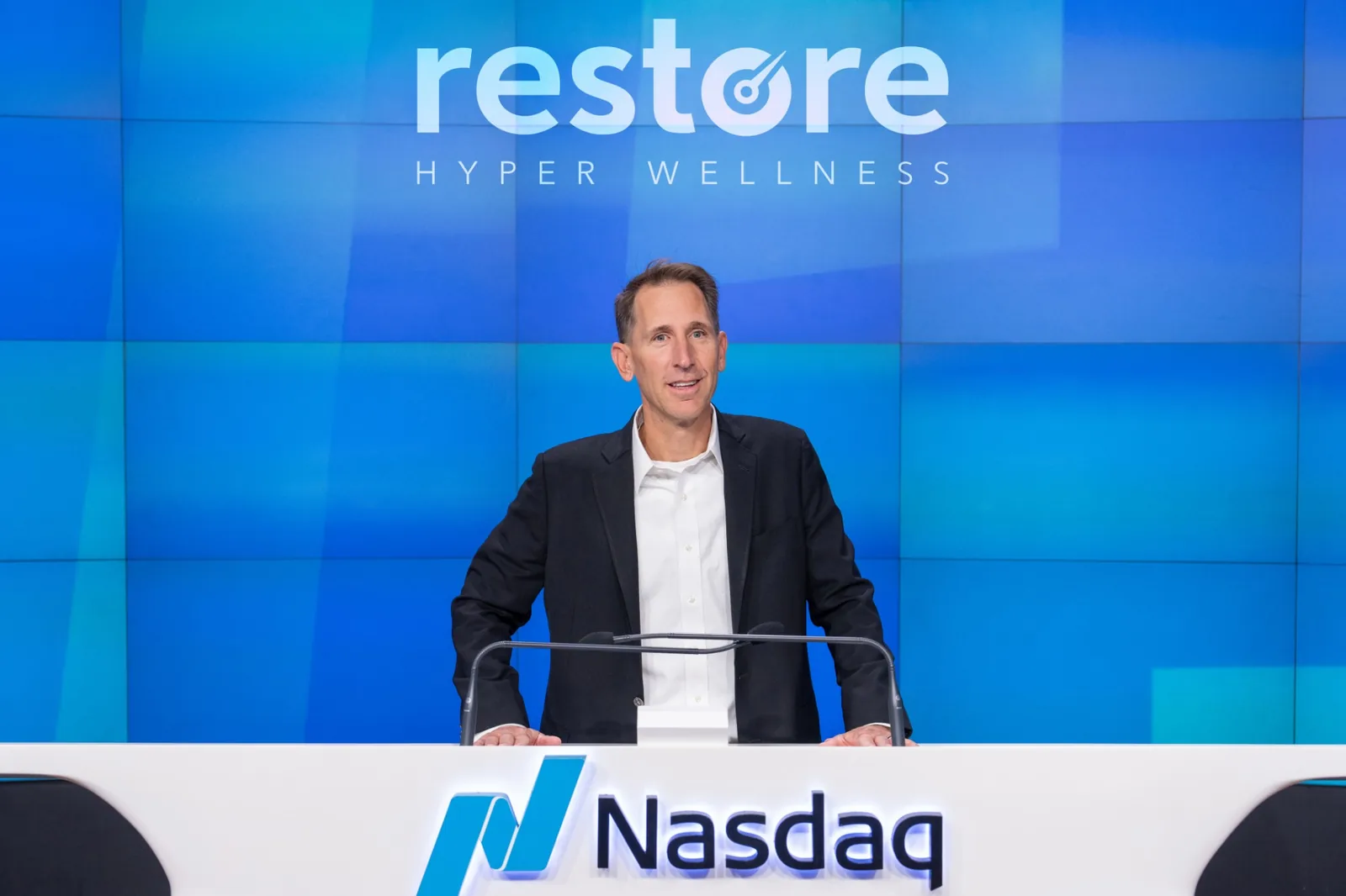 Steve Welch at the Nasdaq podium beneath the Restore Hyper Wellness logo